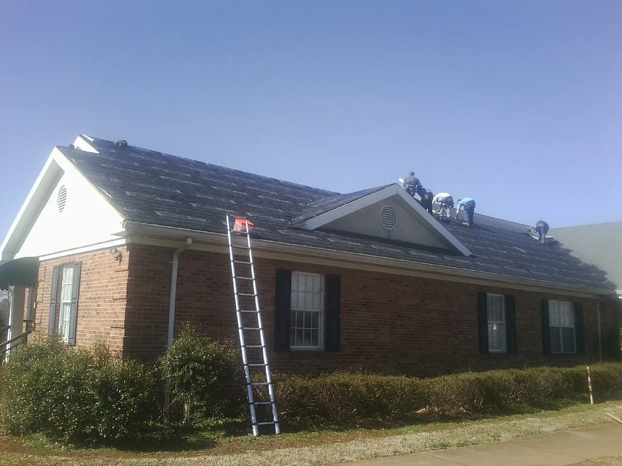 Crew tearing shingles off a brick ranch roof with a ladder set — Metal Roof Repair work by our crew in New Trenton