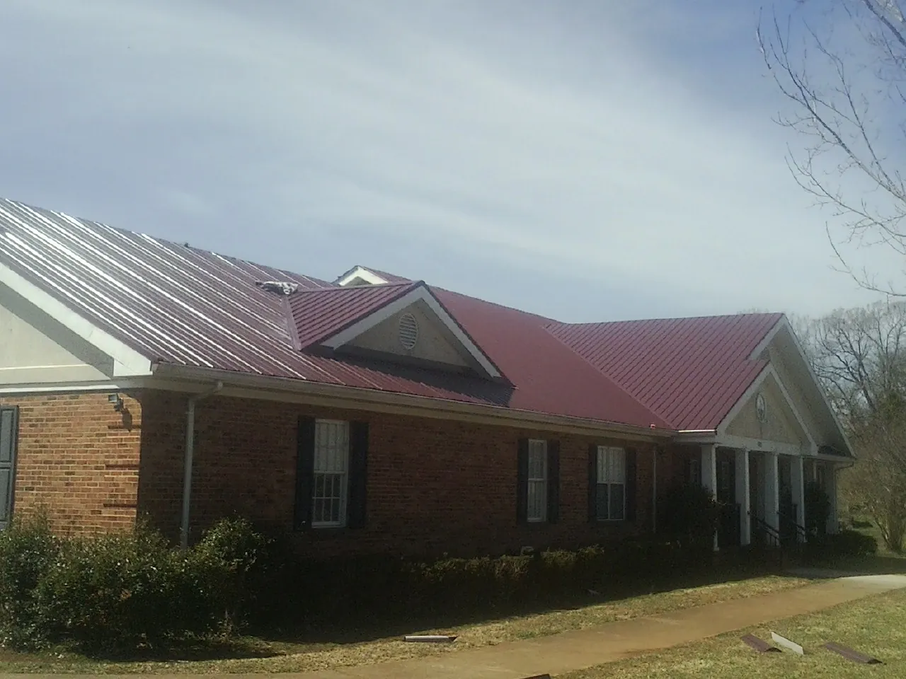 Red metal roof with gabled entries on a long brick building, from a Hail Damage Roof Repair job in New Trenton