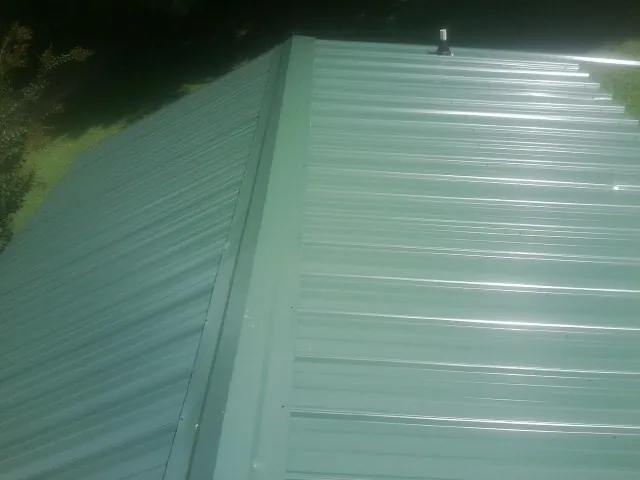 New green metal panels meeting at the ridge of a roof — Flat Roof Repair work by our crew in New Trenton