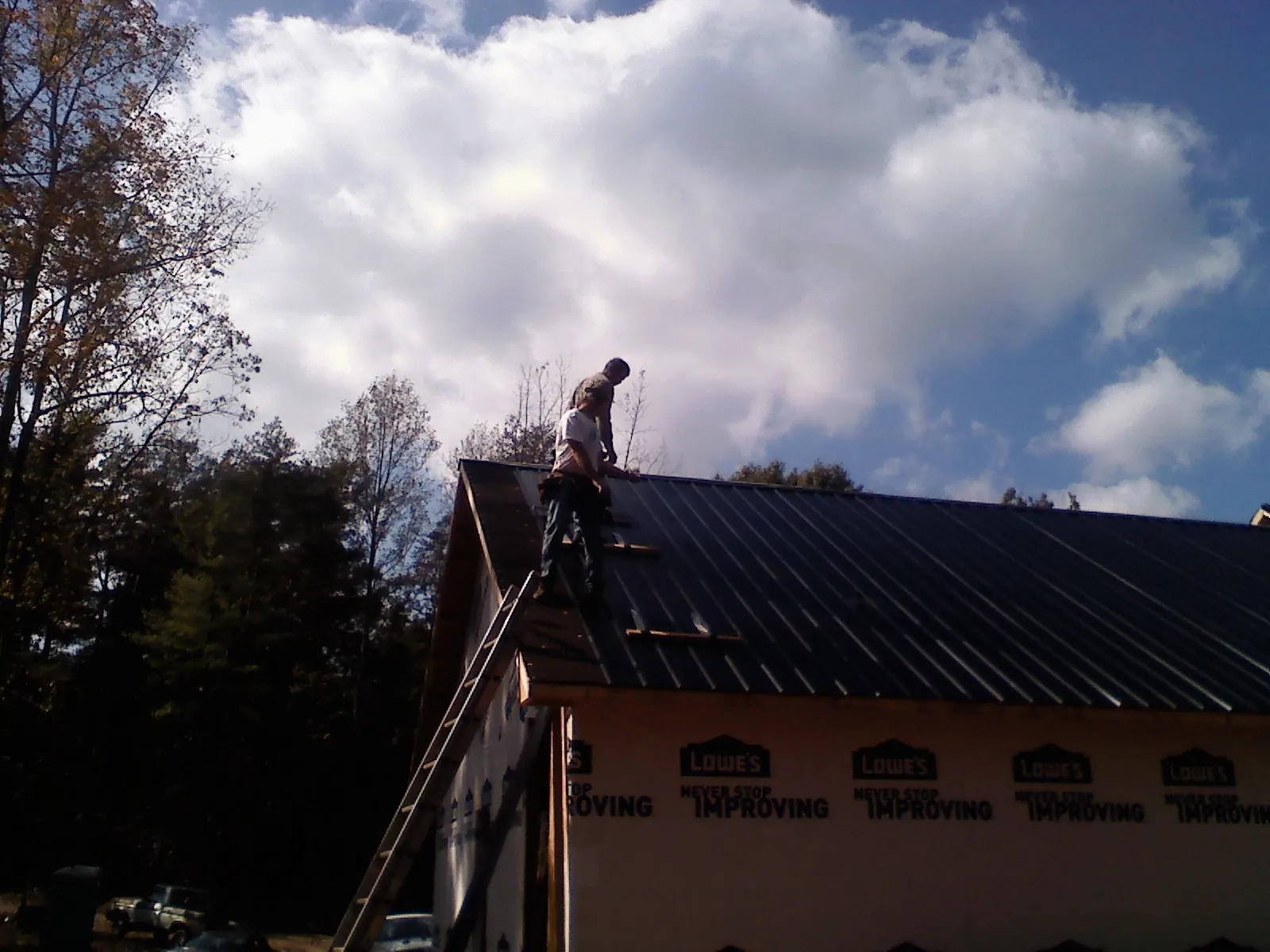 Roofer fastening dark metal panels high against a cloudy sky, from a Roof Inspection job in New Trenton