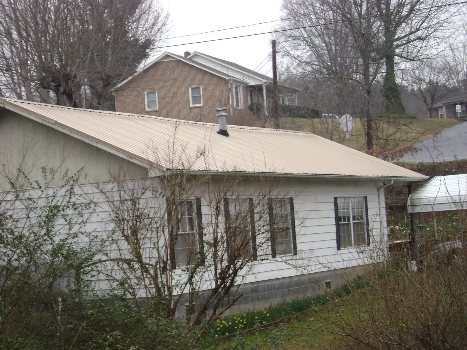 Tan metal roof on a white sided house set into a hillside — Commercial Roofing by Roofing Brothers in New Trenton